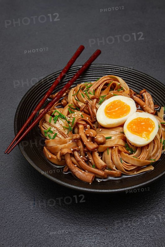 Buckwheat noodles soba with shimeji mushrooms, with boiled egg, green onion, sesame seeds, homemade, on a dark background, without people