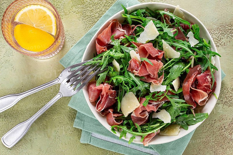 Fresh arugula salad with prosciutto and grated parmesan cheese, on a plate, homemade, no people