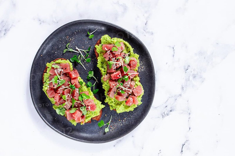 Fresh tuna tartare on avocado spread toast with microgreens served on a black plate