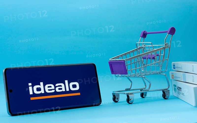 Dhaka, Bangladesh- 03 July 2025: Smartphone with idealo logo next to a small shopping cart and boxes against a blue background
