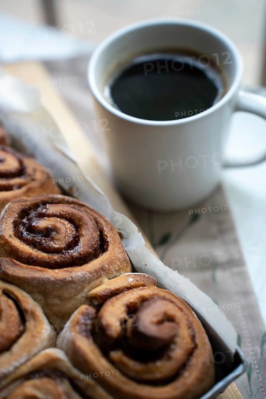 Freshly baked cinnamon rolls on a wooden board with a cup of coffee
