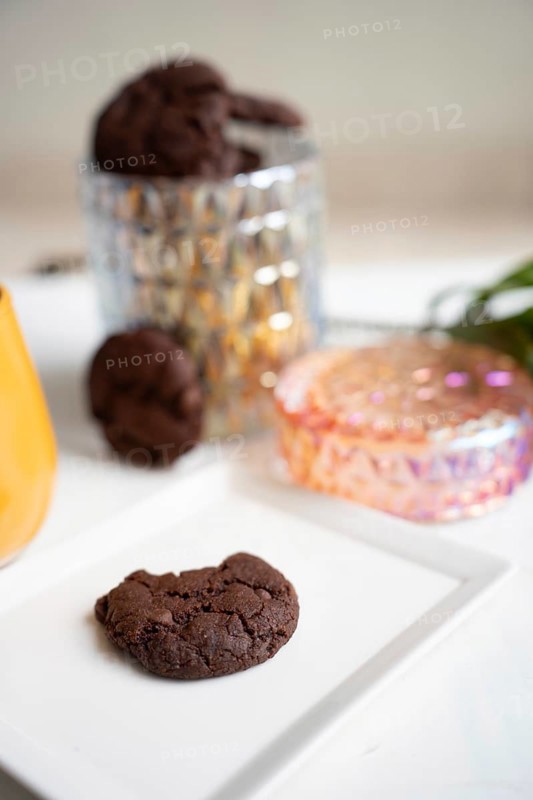 Chocolate chip cookie on white plate, cookie jar in background