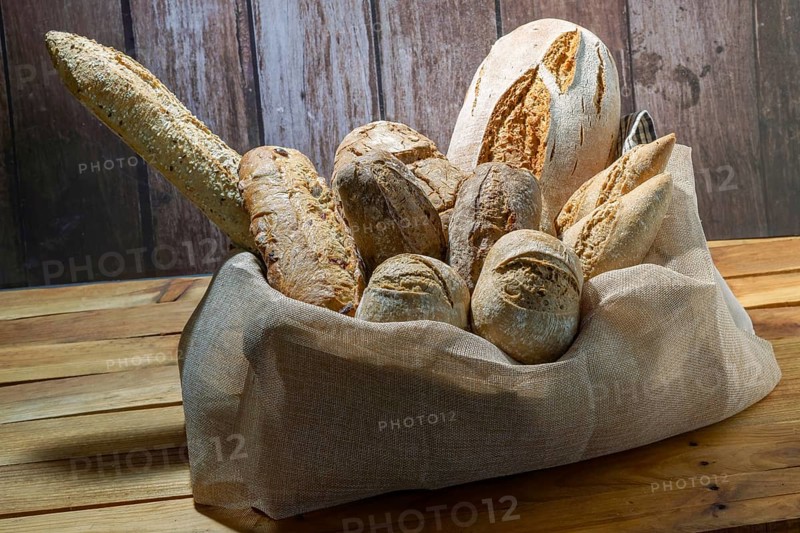 Freshly baked artisanal bread assortment including baguettes and rolls, creating a rustic still life on wood