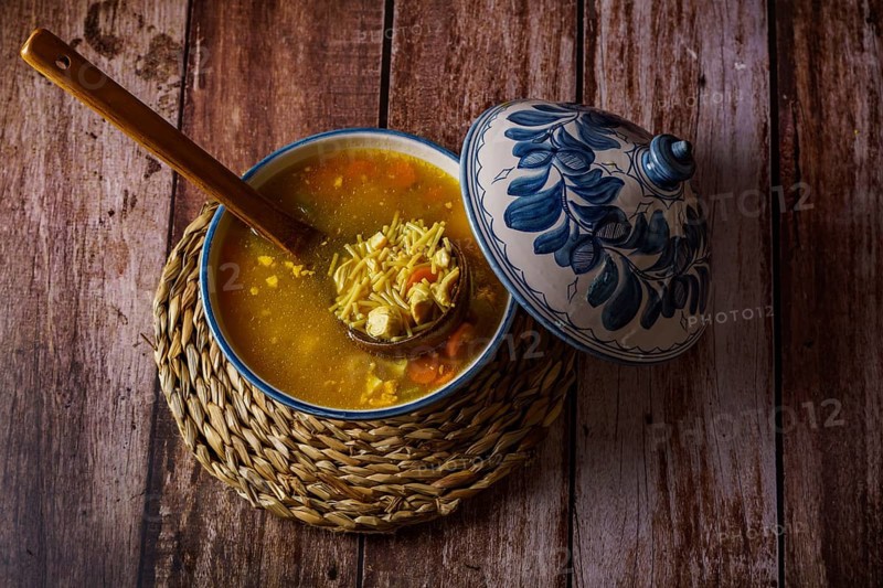 White and blue soup tureen with chicken noodle and vegetable soup with a wooden spoon