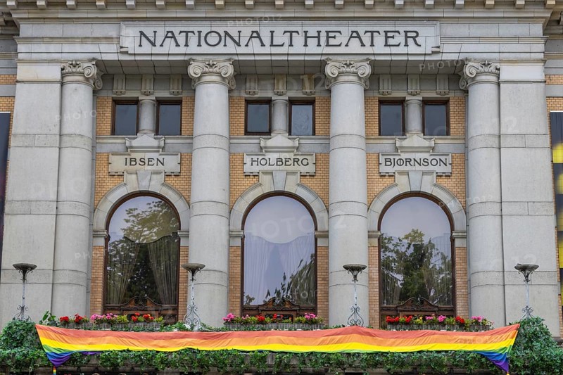 Facade of the National Theatre in Oslo, bearing the names of three Norwegian writers – Ibsen, Holberg and Bjørnson. The rainbow flag, the LGBT pride flag, has been hoisted on the balcony for the Oslo Pride festival. Oslo, Østlandet, Norway