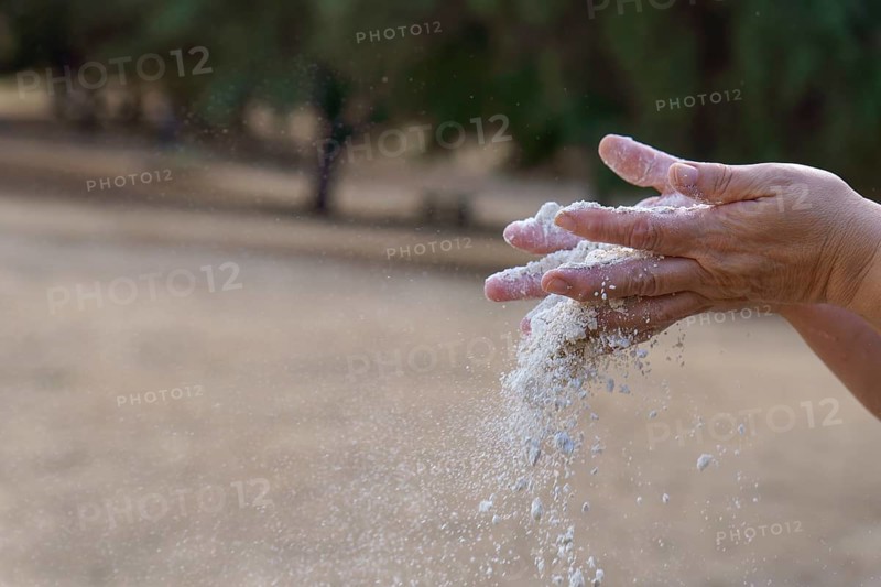 Hands pouring white sand, symbolizing the passage of time, impermanence, and the fleeting moments of life