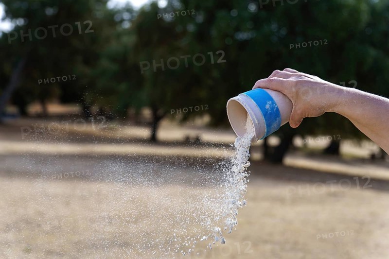 Hand pouring white chalk powder from a container, creating a cloud of dust dispersing in an outdoor setting