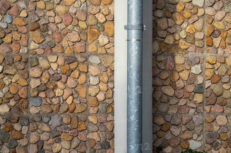 Borken, NRW, Germany, RPebble stone wall with a vertical metal drainpipe creating an interesting pattern and texture