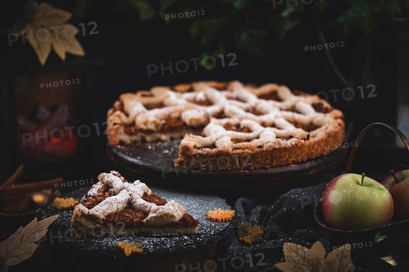 Apple cake with powdered sugar on a dark table with autumn decorations