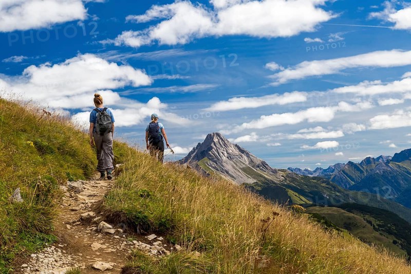 Two hikers on a trail in mountainous landscape under blue sky, Schröcken, Austria
