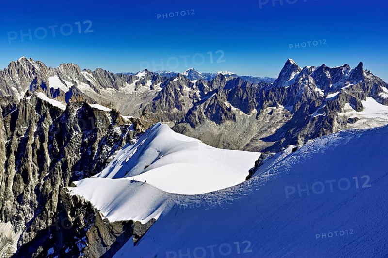 Mountaineers climb over a snow-covered ridge with Grandes Jorasses mountain in the background, Aiguille du Midi mountain station, Chamonix-Mont-Blanc, Haute-Savoie, France