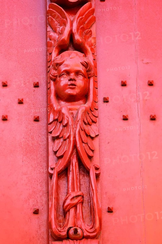 Red wooden door with decorative carving of an angel figure at the entrance to the historic St. Salvator Cathedral, Sint-Salvatorskathedraal, in the old town of Bruges, UNESCO World Heritage Site, Flanders, Belgium
