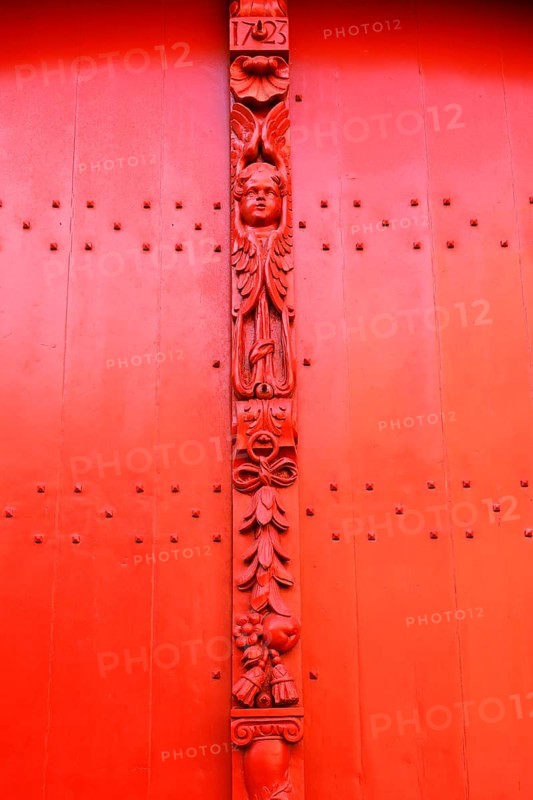 Red wooden door with decorative carvings and an angel figure at the entrance to the historic St. Salvator Cathedral, Sint-Salvatorskathedraal, in the old town of Bruges, UNESCO World Heritage Site, Flanders, Belgium