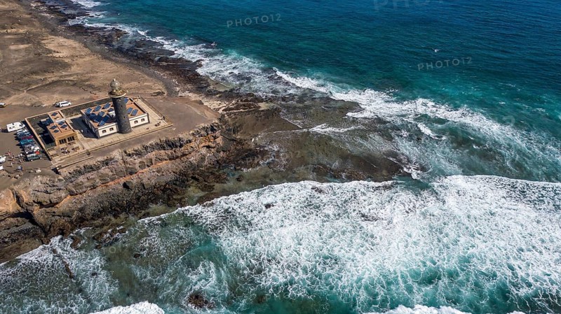 Aerial view from left lighthouse Faro Punta de Jandia at the southern tip of Jandia Peninsula, in the foreground white foam crowns on moving sea swell large high waves on reef edge beaming sea strong surf, Fuerteventura, Canary Islands, Canary Islands, Spain