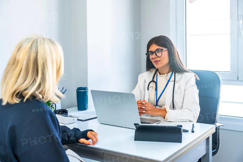 Female doctor in a white lab coat and stethoscope consulting a patient, providing professional medical advice and explaining healthcare information in a modern clinic office