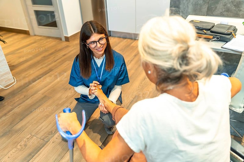 Healthcare professional assisting an elderly patient with physical rehabilitation exercises on her foot, focusing on mobility and recovery during a physiotherapy session