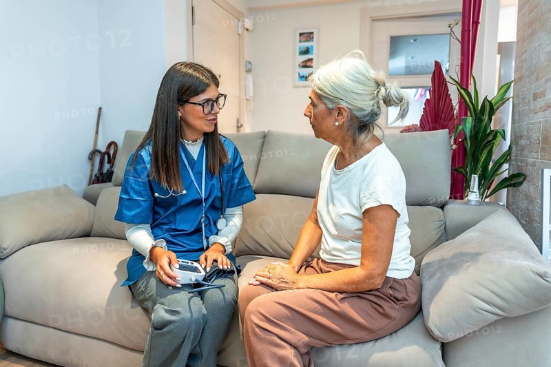 Healthcare professional checking blood pressure for an elderly woman during a home medical visit, providing essential care and support in her residence