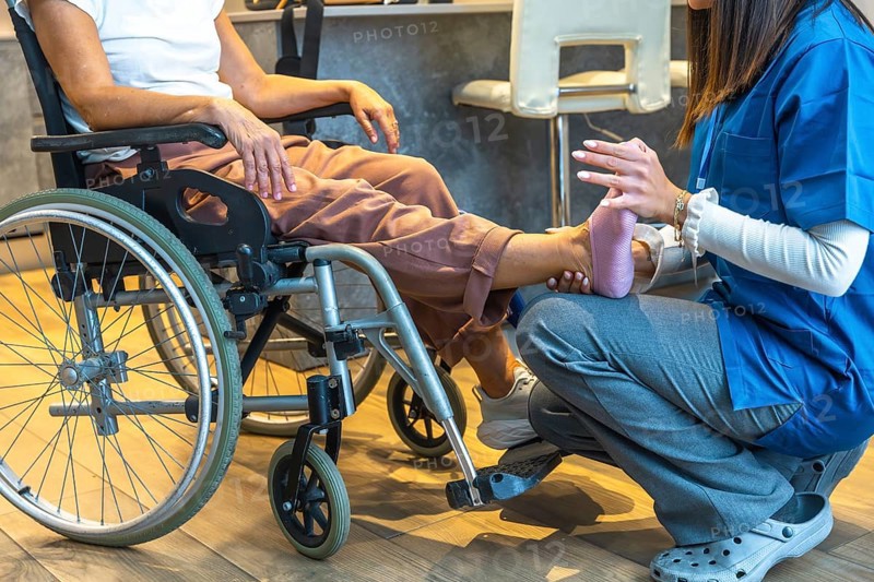 Physiotherapist providing physical therapy to a senior patient sitting in a wheelchair, offering gentle care and support for leg and foot rehabilitation