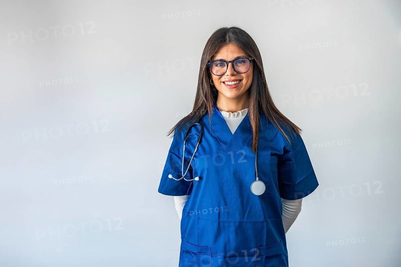 Female doctor in blue scrubs with stethoscope, smiling confidently at camera on white background, professional, friendly healthcare provider representing care and trust in clinical setting