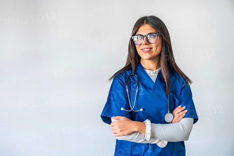 Young woman working as a professional healthcare provider, confidently standing with crossed arms, looking aside and smiling, embodying expertise and medical care