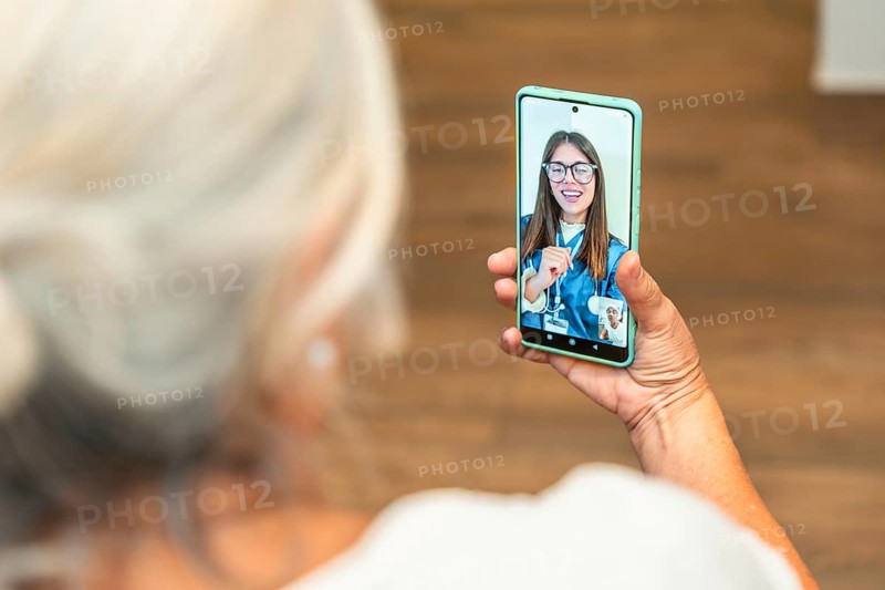 Senior woman is using a smartphone for an online medical consultation, receiving virtual healthcare assistance from a young female doctor on the screen, connecting remotely