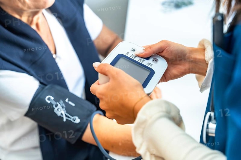 Healthcare professional checking a senior woman's blood pressure at home or in a clinic, focusing on preventive medicine, wellness, and monitoring vital signs for elderly care