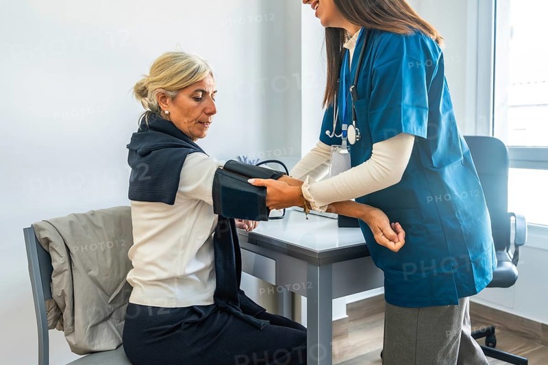 Healthcare professional checking a senior woman's blood pressure. Monitoring her health during a routine medical examination in a bright office environment. Focusing on preventive care and well being