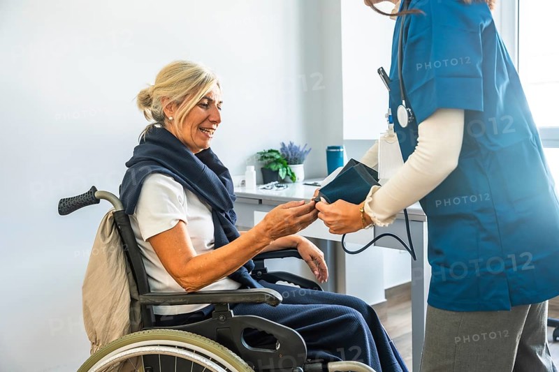 Medical professional checking a senior woman's blood pressure while she is sitting in a wheelchair, providing healthcare and support in a clinic environment
