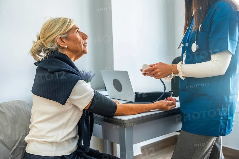 Medical professional monitoring and recording an elderly patient's blood pressure with a sphygmomanometer during a regular health checkup, focusing on preventive healthcare