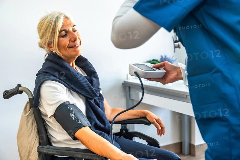 Senior woman in a wheelchair having her blood pressure measured by a medical professional, receiving health care and monitoring vital signs during a regular checkup
