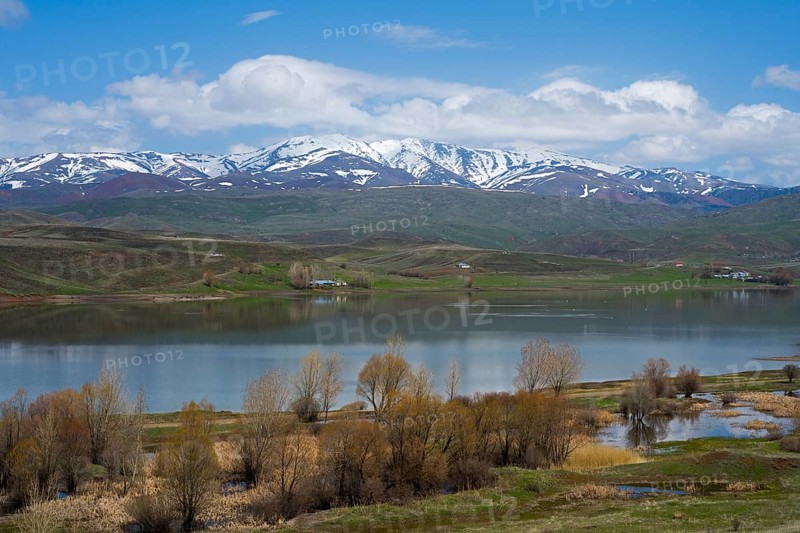 Peaceful landscape with a lake surrounded by snow-capped mountains. Trees and meadows dot the shore under a blue sky with scattered clouds, Imranli Reservoir, Imranli, Kizilirmak River, Kizilirmak, Sivas Province, Turkey