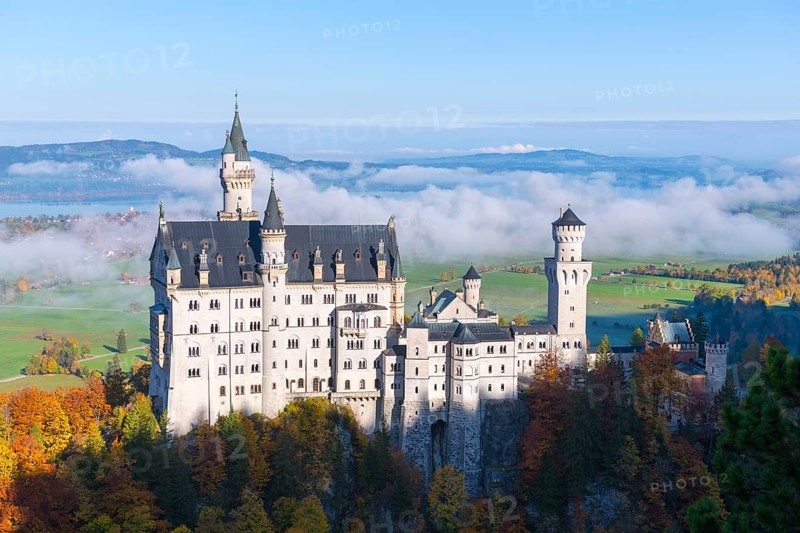 Majestic Neuschwanstein Castle overlooking spring-like valley with clouds and autumn trees, Schwangau near Füssen, Ostallgäu, Allgäu, Bavaria, Germany