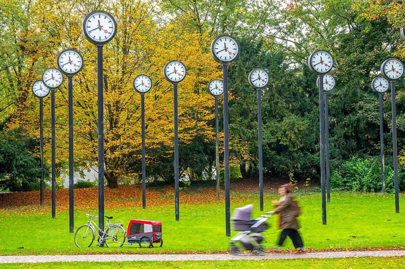 The art installation Zeitfeld in Volksgarten Park in Düsseldorf-Oberbilk, a total of 24 station clocks, on 6 meter high steel columns, have been running synchronously since 1987, walkers in the municipal park, artwork by Düsseldorf artist Klaus Rinke, symbol of time, time change, North Rhine-Westphalia, Germany