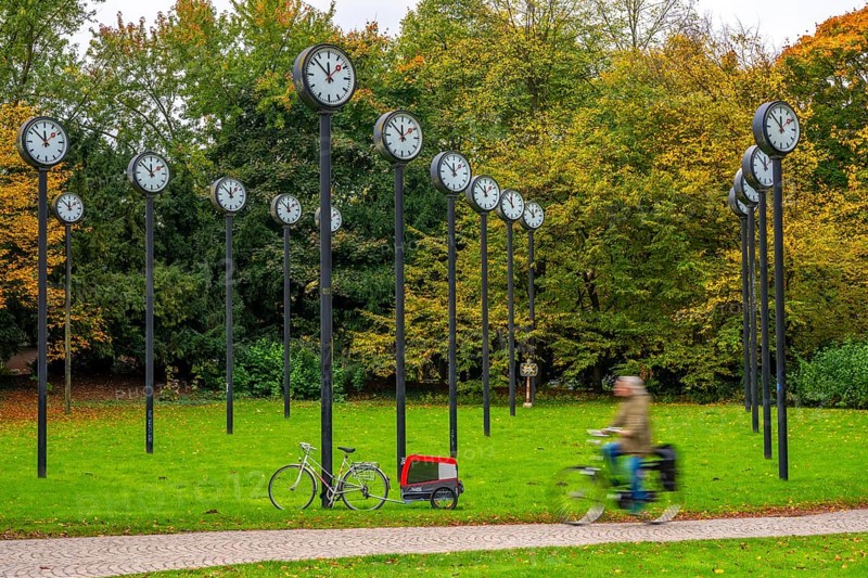 The art installation Zeitfeld in Volksgarten Park in Düsseldorf-Oberbilk, a total of 24 station clocks, on 6 meter high steel columns, have been running synchronously since 1987, cyclists in the municipal park, artwork by Düsseldorf artist Klaus Rinke, symbol of time, time change, North Rhine-Westphalia, Germany