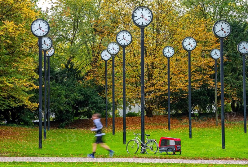 The art installation Zeitfeld in Volksgarten Park in Düsseldorf-Oberbilk, a total of 24 station clocks, on 6 meter high steel columns, have been running synchronously since 1987, jogger in the municipal park, artwork by Düsseldorf artist Klaus Rinke, symbol of time, time change, North Rhine-Westphalia, Germany
