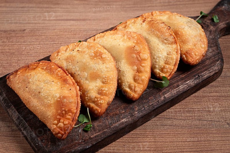 Fried chebureks, deep-fried, mini, on a chopping board, wooden table, close-up, no people