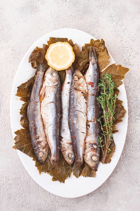 Baked fish, in grape leaves, with spices, on a white plate, homemade