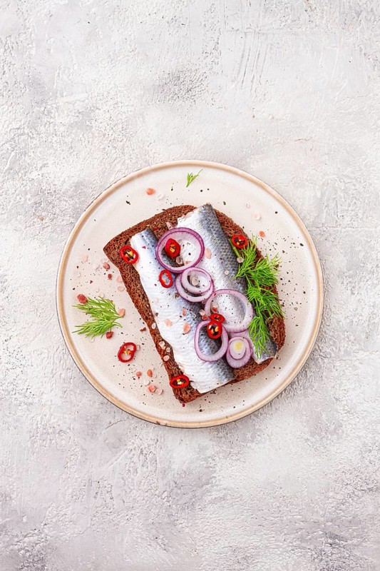 Sandwiches, Herring fish, on dark rye bread, sprinkled with onion, chili pepper and herbs, on a light plate