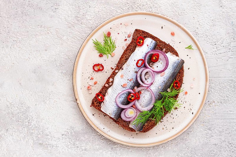 Sandwiches, Herring fish, on dark rye bread, sprinkled with onion, chili pepper and herbs, on a light plate