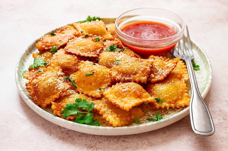 Fried ravioli with parmesan cheese, served with red sauce and garnished with herbs, on a light background, no people