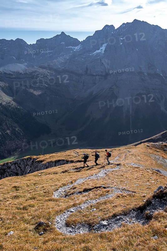 Three hikers descending, hiking trail with serpentines from Gamsjoch, dramatic rock faces of Hochglück in the back, eastern Karwendel, Tyrol, Austria