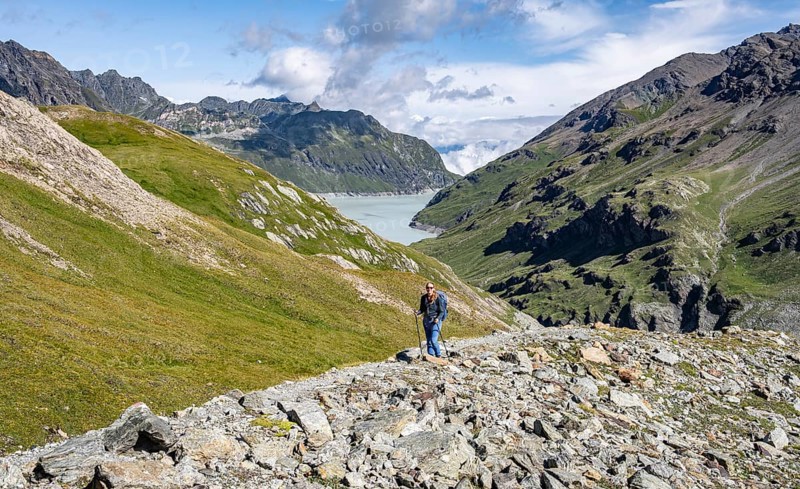 Hiker in a wide mountain landscape with a view of valley and lake, surrounded by green hills, Mont Blanc de Cheilon mountain summit with glacier in the back, Hérménence, Valais Alps, Switzerland