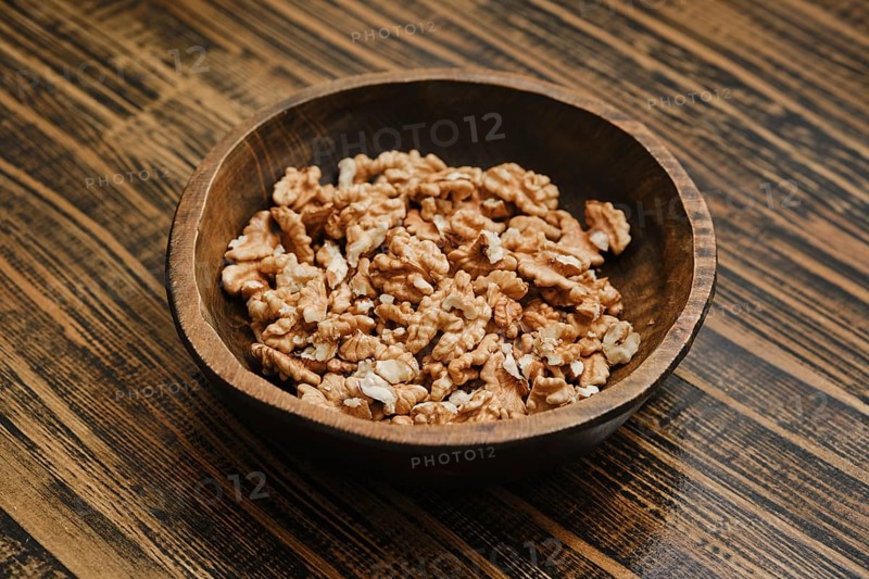 Bowl filled with shelled walnut pieces on a wooden table in a cozy kitchen setting
