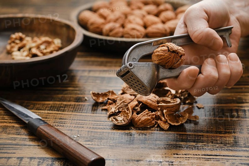 A person uses a nutcracker to open a walnut in a kitchen. There are bowls filled with walnuts shells on a tabletop