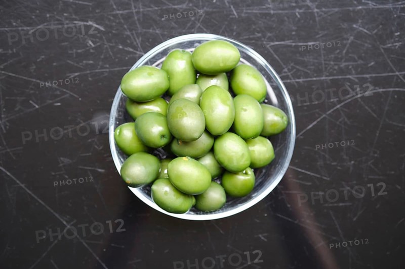 Overhead view of a bowl filled with green olives on a black surface. The olives are vibrant and glossy, showcasing their natural color