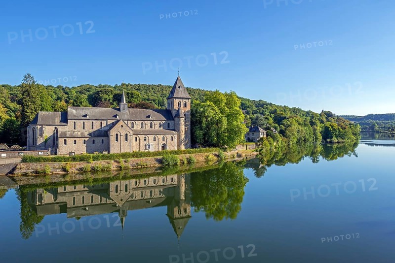 Abbey Church of St Peter, Église abbatiale Saint-Pierre d'Hastière, Hastière-par-delà reflected in water of the river Meuse, Namur, Wallonia, Belgium