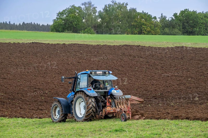 Tractor with plough, agricultural ploughing machine working on a field in autumn, fall in the Belgian Ardennes, Luxembourg, Wallonia, Belgium