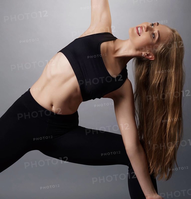 Pretty young fitness trainer in black top and leggings exercising on mat in studio