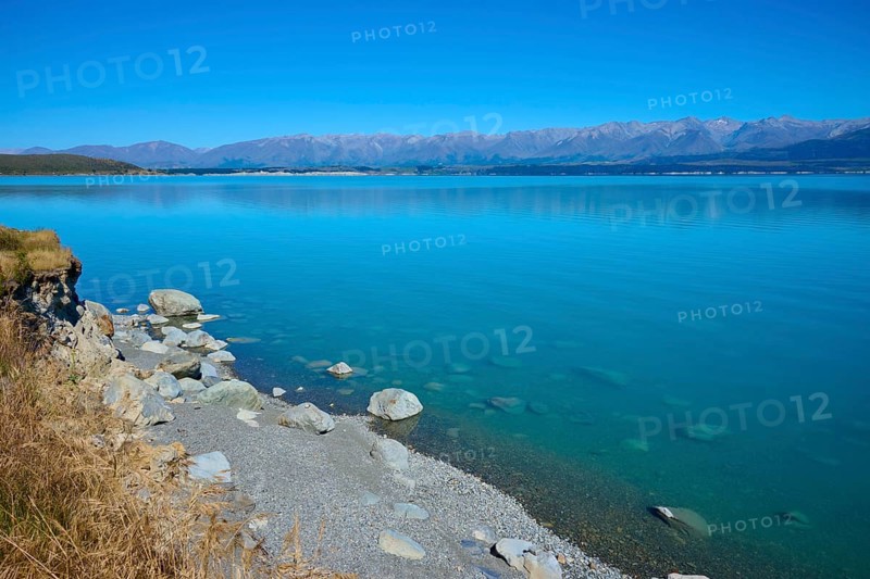 Rocky shore and clear lake with mountain views under clear skies, Lake Pukaki Viewpoint, Pukaki, Canterbury, South Island, New Zealand