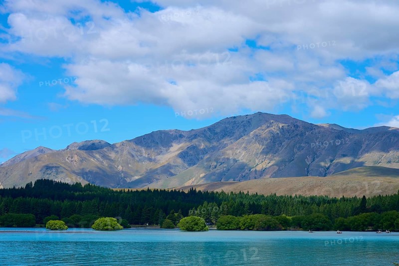 Mountainous landscape with a lake in the foreground and wooded hills under a cloudy sky, Lake Tekapo, Canterbury, South Island, New Zealand